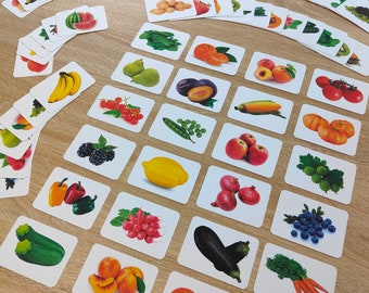 May include: A collection of rectangular educational flashcards featuring colorful illustrations of various fruits and vegetables, including bananas, lemons, eggplants, carrots, berries, and tomatoes, arranged in a scattered grid pattern.