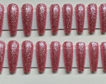 May include: Set of 20 pink glitter coffin-shaped false nails. The nails are arranged in two rows of ten on a white background.
