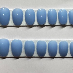 Peut inclure: Deux rangées d'ongles artificiels ovales bleu clair sur un présentoir en mousse blanche.