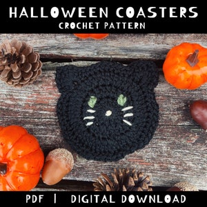 Pu&ograve; includere: Sottobicchiere a forma di gatto in crochet nero con occhi verdi e baffi bianchi. Il sottobicchiere &egrave; su una superficie di legno con una pigna, ghiande e piccole zucche.