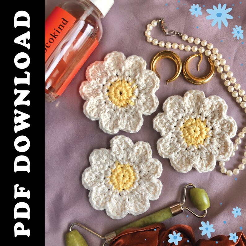 May include: Three handmade crochet daisy coasters with white petals and yellow centres are arranged on a purple surface. A bottle of skincare product, gold earrings, a pearl necklace, and a jade roller are also visible. The image has the text "PDF DOWNLOAD" on the left side.
