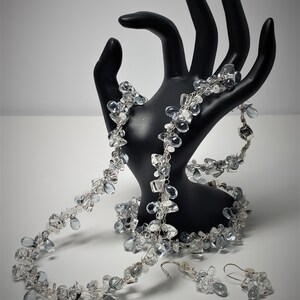 May include: A silver wire wrapped necklace, bracelet, and earrings set with clear and blue teardrop shaped crystals.
