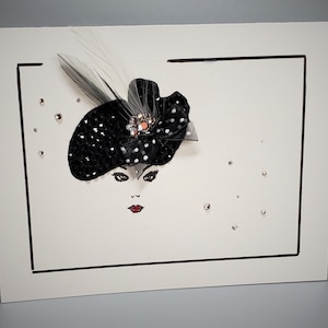 May include: A white card with a black frame around a black and white illustration of a woman wearing a black hat with white polka dots and a feather. The hat has a rhinestone embellishment. There are small silver rhinestones scattered around the illustration.
