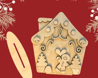 May include: A wooden gingerbread house cutout with a gingerbread person inside. The house has a chimney, candy cane accents, and a heart-shaped window. The cutout is on a red background.