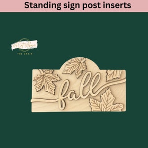 May include: Wooden sign post insert with the word "fall" in a cursive font and a design of maple leaves. The sign is made of light wood and has a rounded top.