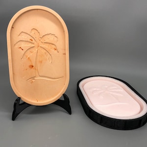 Peut inclure: Un plateau en bois avec un motif de palmier sculpté, présenté sur un support noir. Un plateau assorti avec un motif de palmier rose est présenté à côté.