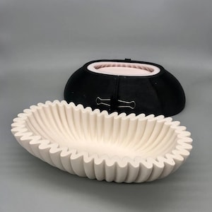 Pode incluir: Uma tigela de cerâmica branca com uma borda canelada. A tigela tem formato oval e um acabamento liso e brilhante.