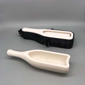 May include: Two-piece ceramic bottle mold. The bottom piece is a cream color, shaped like a bottle with a hollow interior. The top piece is black with a white interior, designed to fit around the bottle shape. Both pieces are on a gray background.
