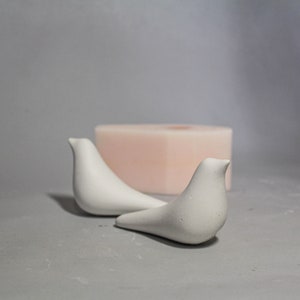 May include: Two white ceramic bird figurines on a grey surface. The birds are facing different directions and have a simple, modern design.