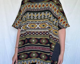 May include: A short-sleeved poncho-style top with a gray turtleneck collar. The top features a geometric pattern in shades of gray, black, yellow, red, and green. A gray patch pocket is on the side. The garment is made of a woven fabric.