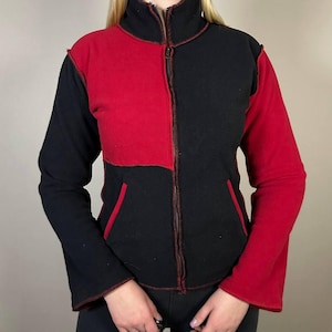 Puede incluir: Chaqueta con cremallera de dos tonos en negro y rojo. La chaqueta presenta un cuello alto, mangas largas y una cremallera completa. Las costuras están acentuadas con pespuntes rojos. La chaqueta tiene dos bolsillos delanteros y un corte holgado.