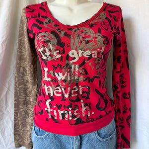 May include: A long-sleeve shirt with a red bodice featuring black abstract patterns and the white text "It's great I will never finish." The right sleeve is brown with a light-colored floral print, while the left sleeve is red with black patterns.