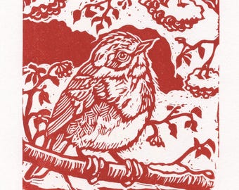 May include: A red and white linocut print of a bird perched on a branch, surrounded by leaves and berries. The bird is detailed with textured lines. The print includes Chinese characters and the artist's initials.