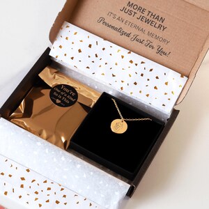 May include: A gold necklace with a round pendant featuring a small engraved image. The necklace is packaged in a black box with a gold foil bag that says "You're One of a Kind So is This". The box is inside a brown cardboard box with the text "More Than Just Jewelry It's an Eternal Memory Personalized Just For You!"