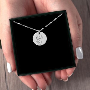 May include: A silver necklace with a round pendant featuring a line drawing of an angel holding a baby.