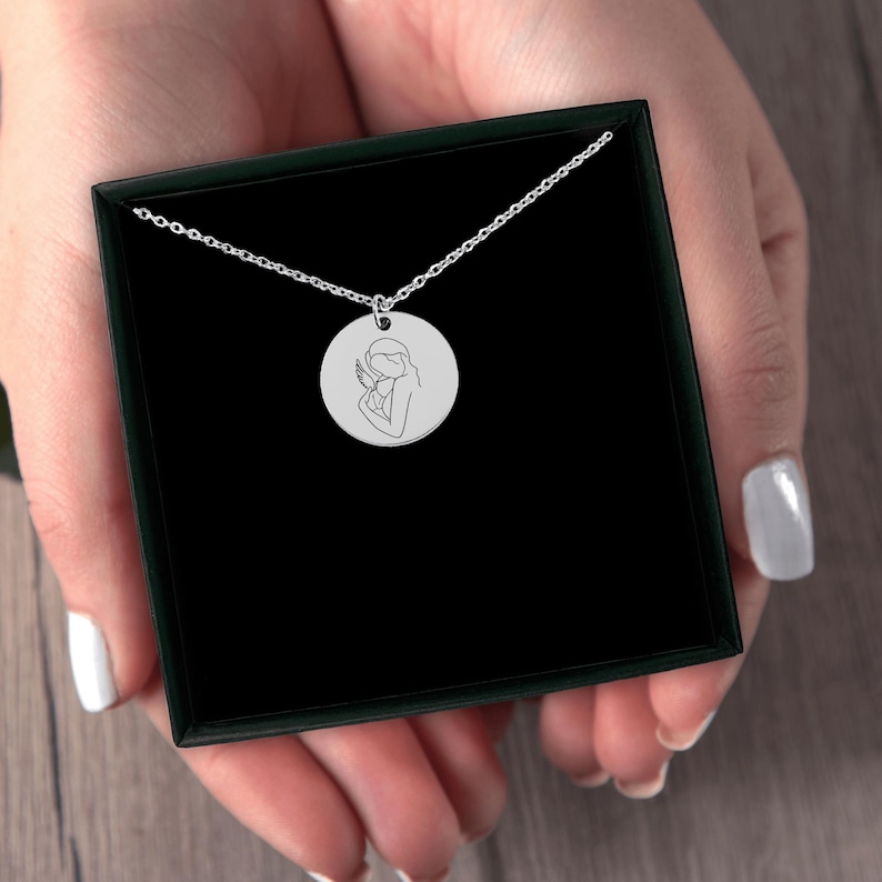 May include: A silver necklace with a round pendant featuring a line drawing of an angel holding a baby.