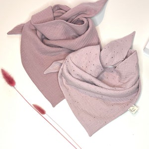 Puede incluir: Dos baberos de muselina rosa para bebé, uno liso y otro con puntos de purpurina dorada. Los baberos están doblados y dispuestos sobre una superficie blanca.