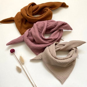 Puede incluir: Tres pañuelos de bandana de muselina de algodón en diferentes colores: marrón, rosa y beige. Los pañuelos están doblados y dispuestos sobre un fondo blanco.