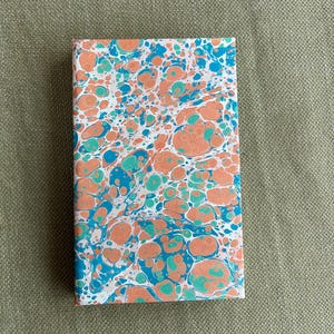 May include: A closed rectangular notebook with a marbled cover. The cover has a pattern of orange, teal, and blue swirls on a white background. The notebook is new.