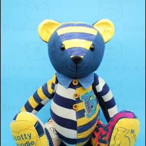 May include: A handmade teddy bear with a patchwork design. The bear features a blue head, yellow and blue striped ears, and a blue and white striped body. The bear has a denim collar and a patch with the letter "B". The bear's feet are yellow with text and a drawing.