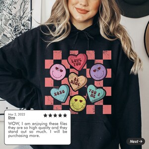 May include: Black hoodie with a pink and white checkered pattern and colorful candy hearts with Valentine's Day messages. The hearts say "Love You", "Be Mine", "XOXO", "You & Me".