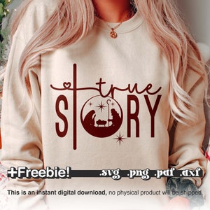 May include: A beige sweatshirt with a maroon graphic that reads "true story." The design includes a cross, a heart, and a circular image of the nativity scene. Below the graphic are the words "+Freebie!" and file type extensions.