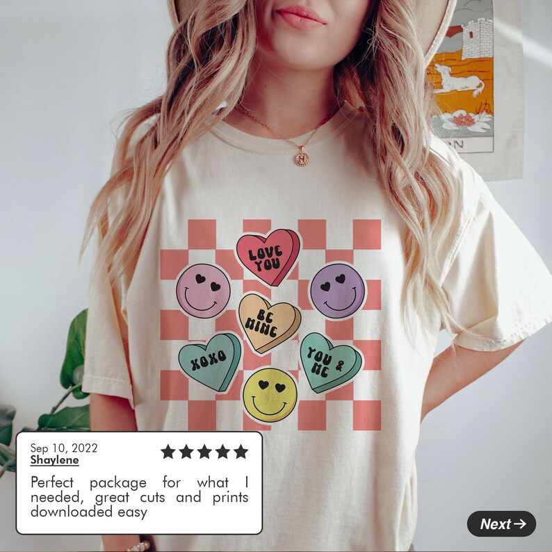 May include: A white t-shirt with a pink and white checkered pattern and colorful heart-shaped candy graphics with smiley faces and text that says "Love You", "Be Mine", "XOXO", and "You & Me".