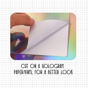 May include: A close-up of a holographic paper or vinyl sheet with a white backing. The backing is being peeled back to reveal the iridescent holographic surface. The text "CUT ON A HOLOGRAM PAPER/VINYL FOR A BETTER LOOK" is printed below the image.