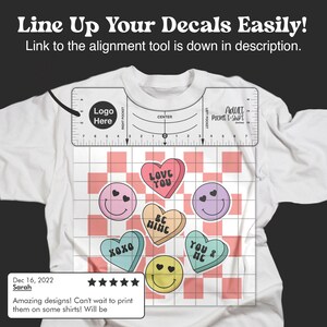 May include: A white t-shirt with a grid pattern and five iron-on decals. The decals are heart-shaped and feature various phrases like "Love You", "Be Mine", "XOXO", and "You & Me". The t-shirt also has a ruler with the words "Adult Pocket T-Shirt" and "Logo Here".