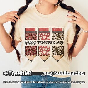 May include: A beige t-shirt with a sublimation design of three pencils. Each pencil has a different pattern: leopard print, white hearts, and leopard print. The text "Happy Valentine's Day" is printed on the shirt.