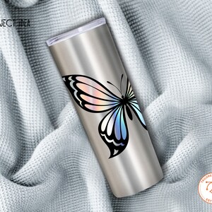 May include: A stainless steel tumbler with a holographic butterfly design. The butterfly has iridescent wings with shades of pink, blue, and purple. The tumbler is on a white fabric background.