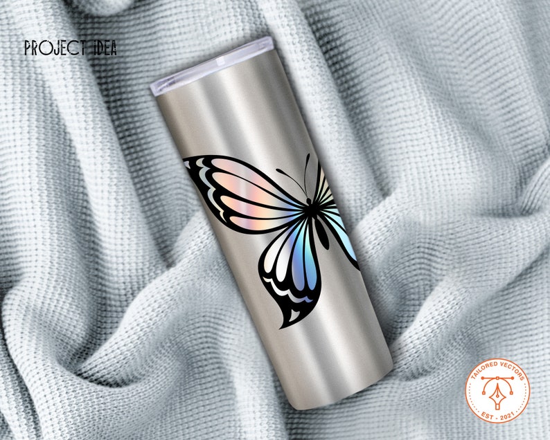 May include: A stainless steel tumbler with a holographic butterfly design. The butterfly has iridescent wings with shades of pink, blue, and purple. The tumbler is on a white fabric background.