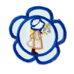 May include: A blue and white embroidered flower patch with a girl in a blue hat and dress holding a bouquet of flowers.
