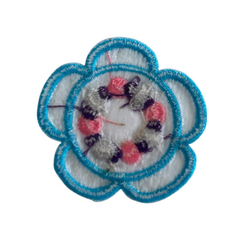 May include: A blue flower-shaped embroidered patch with a white center and a pink and gray swirl design.