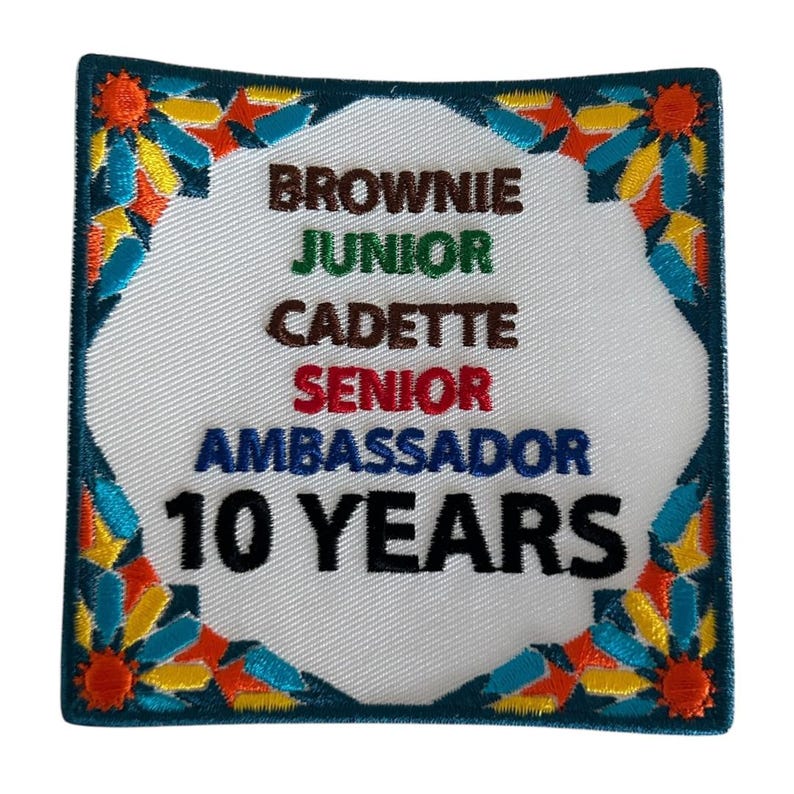 May include: White embroidered patch with a colorful border. The patch says "Brownie, Junior, Cadette, Senior, Ambassador, 10 Years".