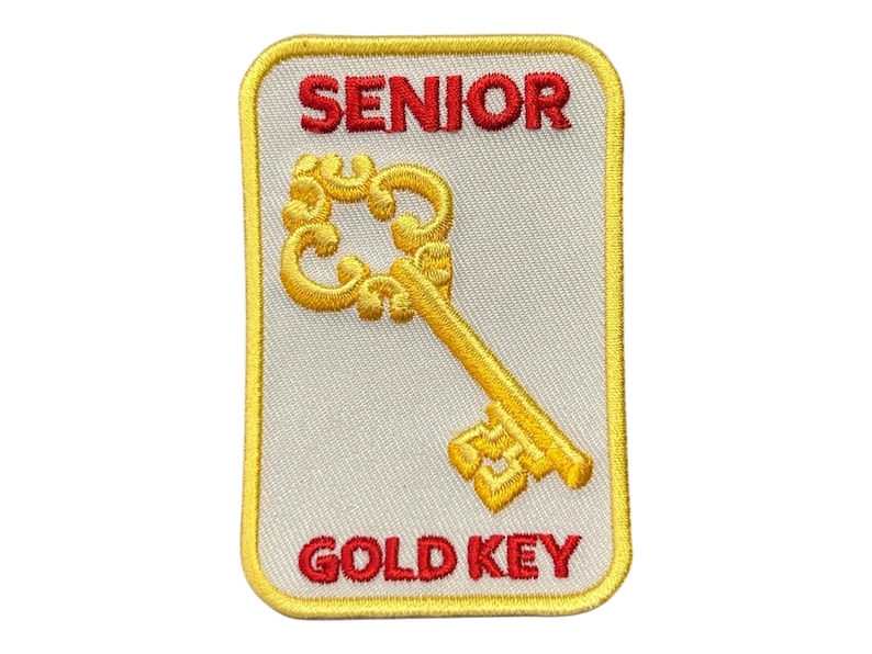 May include: A white patch with a yellow border, featuring a gold key and the text "SENIOR GOLD KEY" in red.