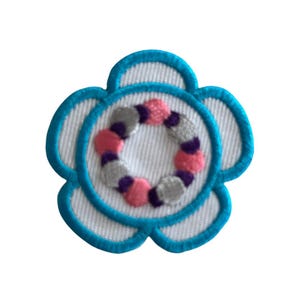 May include: A white flower-shaped patch with a blue outline. The center of the flower has a circle of pink, purple, and gray embroidered shapes.