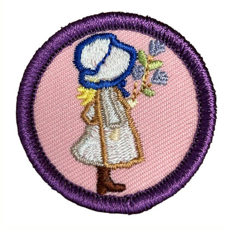 May include: A purple and pink embroidered patch featuring a girl in a white dress and blue bonnet holding a bouquet of flowers.
