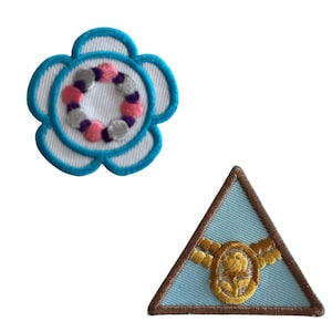May include: Two embroidered patches, one a blue flower with a pink and gray circle in the center, and the other a blue triangle with a gold rope and rose design.