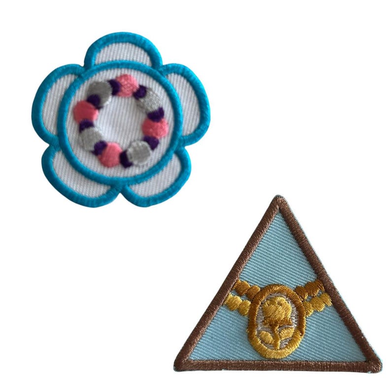 May include: Two embroidered patches, one a blue flower with a pink and gray circle in the center, and the other a blue triangle with a gold rope and rose design.