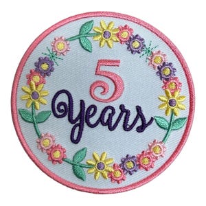 May include: Embroidered patch with a light blue background, featuring the number "5" and the word "Years" in pink and purple script. A wreath of colorful flowers in yellow, pink, and purple surrounds the text, with a pink border.