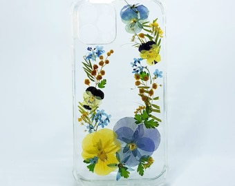 May include: A clear phone case with pressed flowers. The flowers are blue, yellow, and green. The case is designed for a phone with a camera bump.