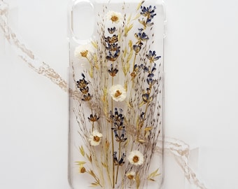 May include: A clear phone case with dried flowers pressed inside. The flowers are white and blue, and they are arranged in a bouquet-like shape.