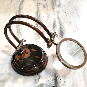 May include: A classic magnifying glass with a dark brown wooden base and frame. The circular lens is held by a metal frame, and the arm is curved. The base has a layered design. The text "Crafts and Engraving" is visible.