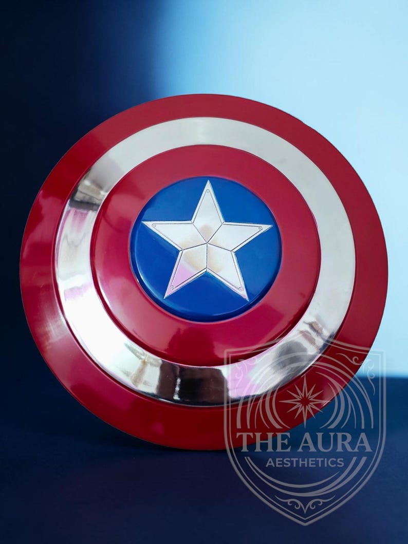 May include: A Captain America shield replica. The shield is circular, featuring a red outer ring, a silver inner ring, and a blue central disc with a silver star. The shield has a glossy finish and is set against a dark blue backdrop.