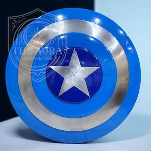 May include: A blue and silver shield featuring a white star at its centre. The shield has concentric circles of blue and silver. The text "THE AURA AESTHETICS" is visible on the shield.