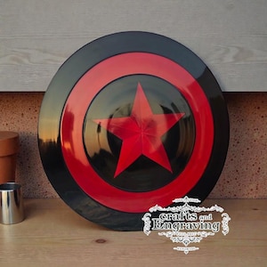 Puede incluir: Un escudo negro y rojo con una gran estrella roja en el centro. El escudo tiene un diseño circular con un anillo rojo y un borde exterior negro. El escudo está hecho a mano y tiene el texto "crafts and Engraving".