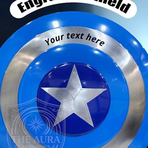 May include: A blue and silver shield with a large silver star in the centre. The shield has the text "Engraved shield" and "Your text here". The logo "THE AURA AESTHETICS" is at the bottom.