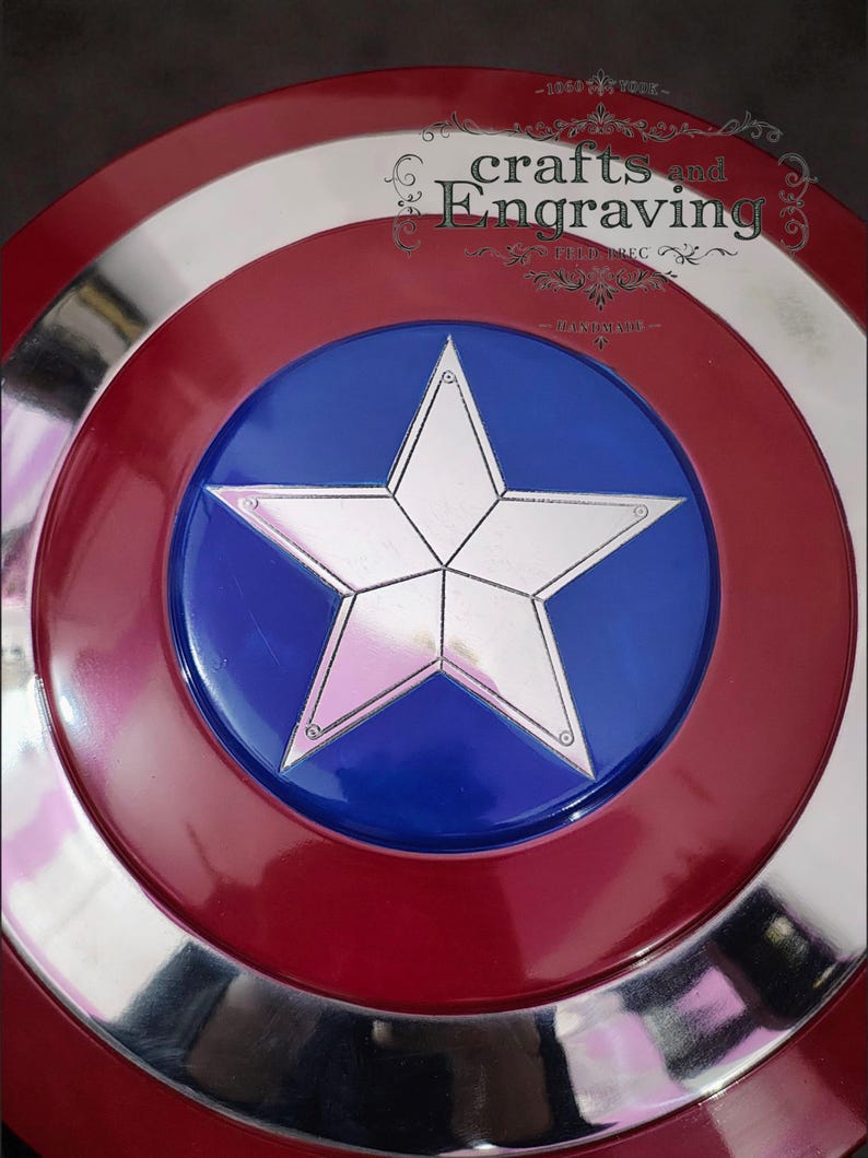 Puede incluir: Una r&eacute;plica del escudo del Capit&aacute;n Am&eacute;rica. El escudo presenta un dise&ntilde;o rojo, blanco y plateado con un disco central azul. Una estrella plateada de cinco puntas est&aacute; centrada en el disco azul. El escudo tiene el texto "crafts and engraving".