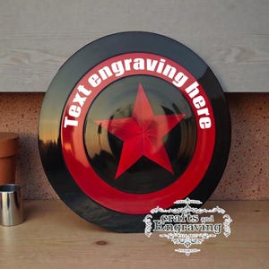 Puede incluir: Un escudo negro y rojo con una gran estrella roja en el centro. El escudo tiene el texto "Text engraving here" en blanco. El escudo es un artículo hecho a mano.